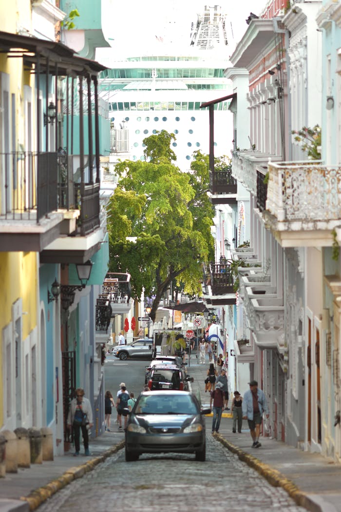 service-02 A lively street scene in San Juan with vibrant buildings and a towering cruise ship in the background.